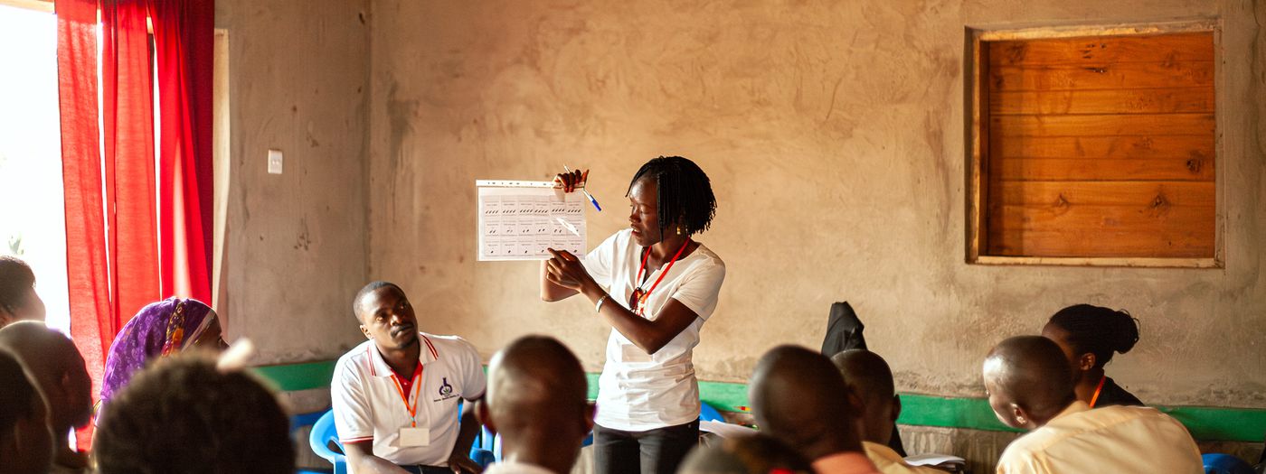 A researcher holds up a chart for participants seated in a classroom in Masaka, Uganda.
